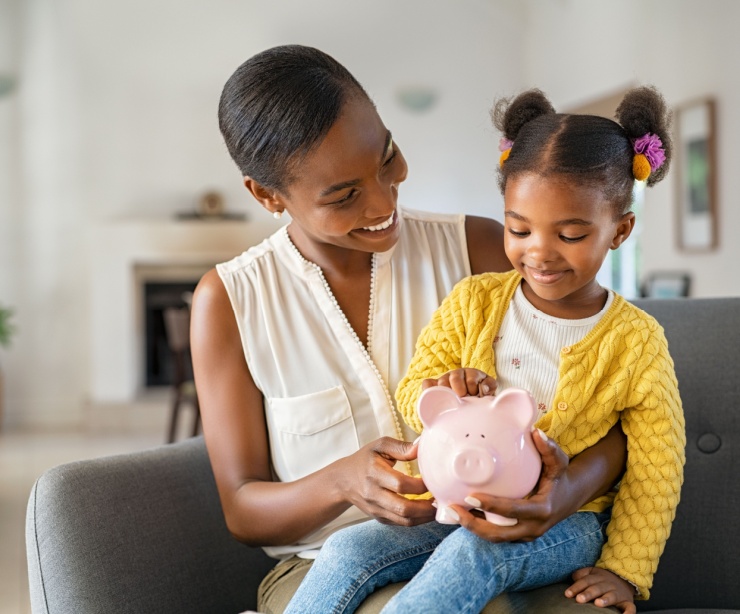 A woman with her child on her knee holding a piggy bank.