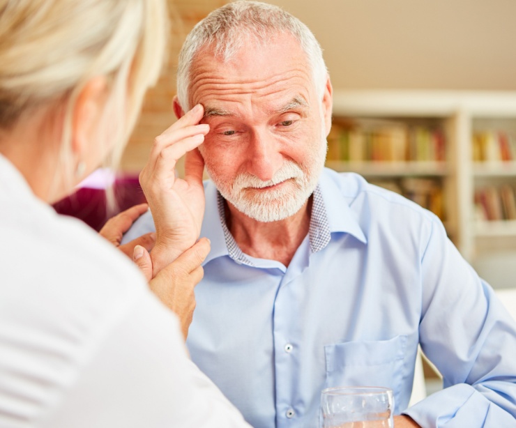 An older man touching his head in confusion while a doctor comforts him.