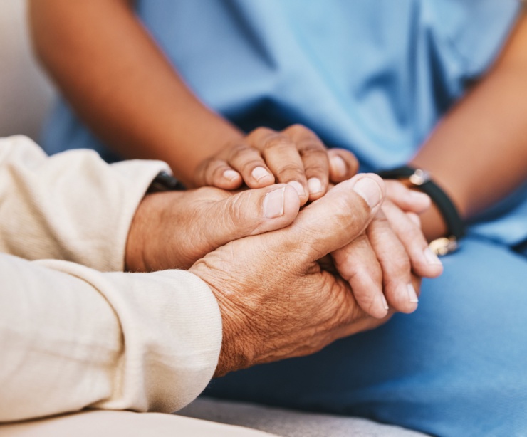 An elderly person holding hands with a nurse.