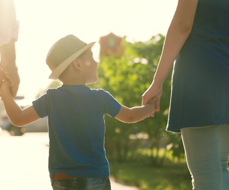 A family with a young child holding hands outdoors.