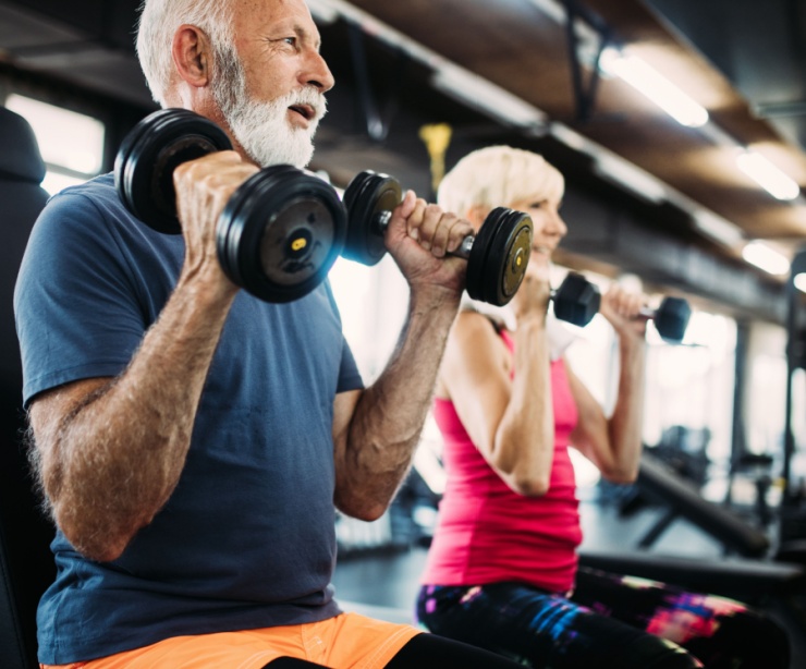 Two people in their 60s using weights in a gym.